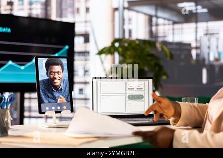 Businesswoman in teleconference call with man, analyzing market trends and data in office. Entrepreneur using tablet to do videocall with expert, developing trading strategies and algorithms Stock Photo
