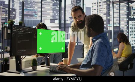 Admin doing software debugging on green screen PC, asking for help from coworker, checking errors in code. Worker fixing coding mistakes on mockup computer, being assisted by colleague, camera B Stock Photo