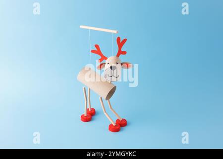 DIY reindeer puppet made from cardboard tubes, red bottle caps, and paper details. Studio shot on a blue background. Christmas craft and holiday decor Stock Photo