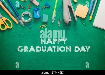 A green chalkboard with a variety of office supplies and the words Happy Graduation Day written on it Stock Photo