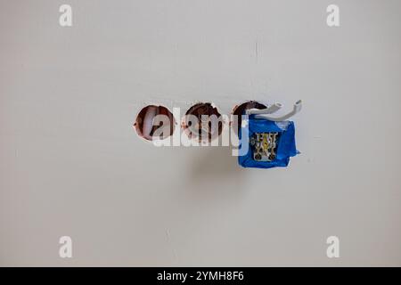 Electrical socket installation in progress with exposed wires and junction box covered in protective tape on white plastered wall. Stock Photo