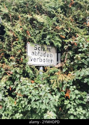 A sign is hidden behind a bush. The sign says dumping of garbage is prohibited in German Stock Photo