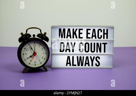 Make each day count always text on LED lightbox with alarm clock on purple background Stock Photo