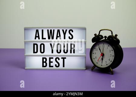 Always do your best text on LED lightbox with alarm clock on purple background Stock Photo