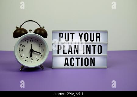 Put Your Plan Into Action text on light box with alarm clock on purple background Stock Photo