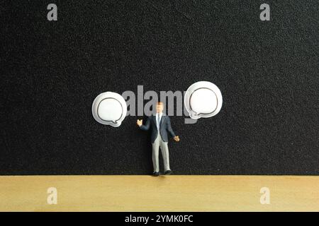 Miniature people toy figure photography. Business choice concept. A businessman standing on blackboard in between two blank bubble message. Isolated o Stock Photo