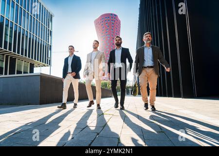 Four confident businessmen walking outdoors in a modern cityscape, dressed in formal suits, casting long shadows, exuding professionalism, teamwork, and leadership in an urban business environment. High quality photo Stock Photo