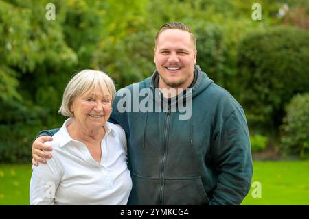 A warm and joyful portrait featuring a young man and an older woman standing together in a lush green garden. Stock Photo