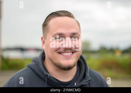 A close-up portrait of a man in a dark hoodie, smiling warmly with a friendly and approachable expression. Stock Photo