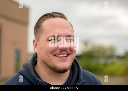 A cheerful close-up portrait of a smiling man in a dark hoodie. His neatly styled hair and light stubble highlight his warm and friendly expression. Stock Photo