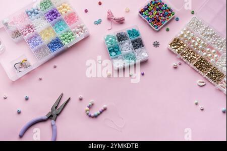 A workspace filled with an array of colorful beads, pliers, and string, all set on a soft pink background. The items are organized in clear containers Stock Photo