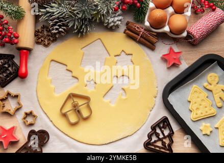 Christmas baking preparation with cookie cutters, dough, eggs, cinnamon sticks, rolling pin and candle on wooden table Stock Photo