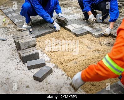 Workers laying brick pavers on the sidewalk.  Road paving and maintenance. Stock Photo