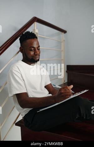 African American Man Writing Notes on Stairs Stock Photo