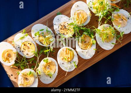 A tray of egg salad with parsley and black pepper. The eggs are cut in half and arranged on a wooden board Stock Photo