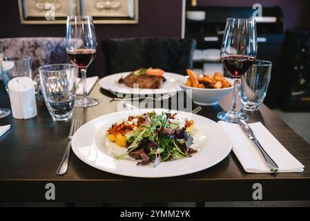 A table with a plate of food and wine glasses. The table setting is elegant and sophisticated. The food on the plate is a salad with meat and potatoes Stock Photo