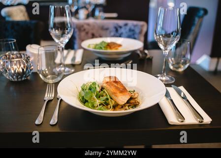 A table with a plate of food and two wine glasses. The table setting is elegant and sophisticated, with a variety of utensils and glasses. Scene is on Stock Photo