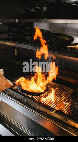 A person is cooking food on a grill with flames. The flames are orange and are rising from the grill Stock Photo