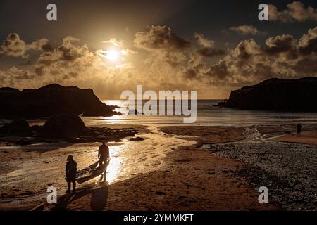 Couple carrying kayak at sunset on the beach at Porth Dafarch, Anglesey, North Wales Stock Photo