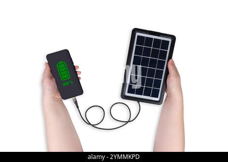 Portable solar panel in one hand connected to smartphone in other hand. Battery charge indicator (100%) is shown on smartphone screen Stock Photo