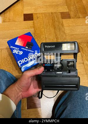 Kyiv, Ukraine - November 22, 2024: A person holds a classic Polaroid instant camera with its original box nearby, placed on a wooden floor, evoking no Stock Photo