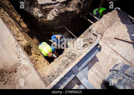 Above view on workers, riggers in trench as they assembly a new plastic HDPE pipeline, elbow of the underground water supply network. Stock Photo