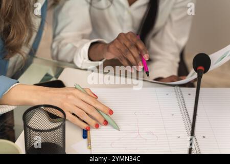 Close up detail of diverse female hands writing in notebook, showing professional manicure and office supplies on modern desk during business meeting. Stock Photo