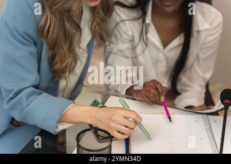 Close-up view of diverse businesswomen hands taking notes during corporate meeting, showing attention to detail and professional collaboration in mode Stock Photo