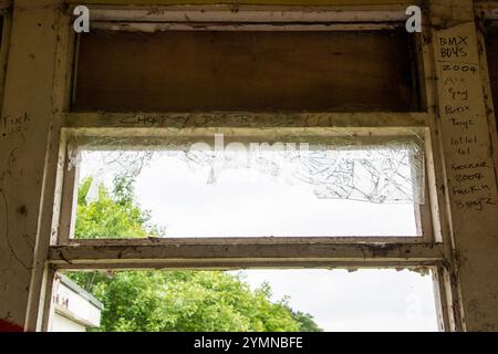 Yorkshire, UK : 31 May 2024 – A window pane, broken and covered with graffiti, in an abandoned building Stock Photo