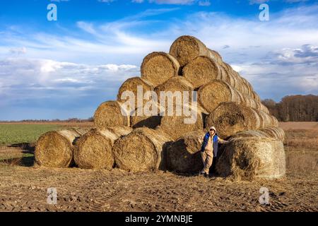 Woman standing in front of a large pyramid of straw bales Stock Photo