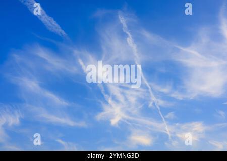 White cirrus clouds and contrails of planes crossing the sky. Bright blue background. Stock Photo
