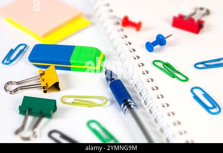 A variety of stationery items, like an eraser, paper clips, and a notebook, are neatly laid out on a clean workspace for school projects. Stock Photo