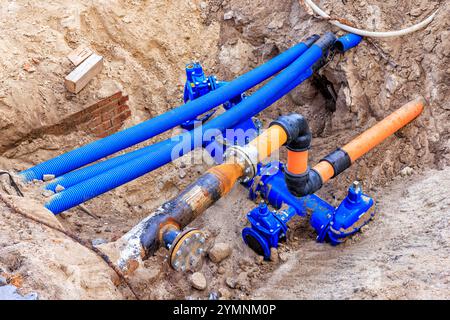 Blue and orange water pipes and cable conduits in a pit. Repair work is underway on city utilities Stock Photo