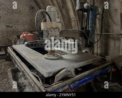 A stone-cutting machine in an industrial workshop, surrounded by dust and equipment, showing a rugged workspace for manufacturing or crafting heavy ma Stock Photo