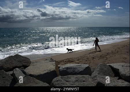 A man walks his dog on a sandy shore near the Mediterranean Sea Stock Photo
