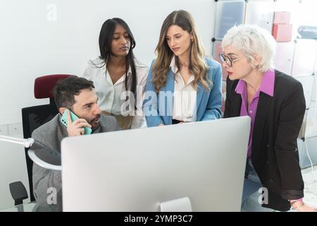 Multi-ethnic business team of four professionals collaborating and discussing project while gathered around computer screen in bright modern office sp Stock Photo