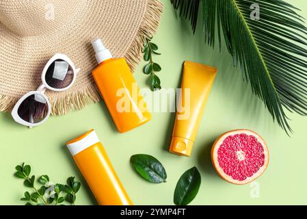 Orange sunblock package, sunglasses, straw hat and palm leaves on green tropical background. Summer vacation and skin care concept, spf uv-protect cos Stock Photo