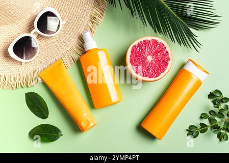 Orange sunblock products, sunglasses, straw hat and palm leaves on green tropical background. Summer vacation and skin care concept, spf uv-protect co Stock Photo