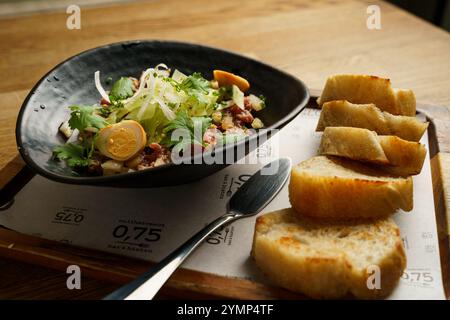 A close-up of a gourmet beef tartare dish served in a black bowl with fresh herbs, garnished with quail eggs and onions, alongside several slices of t Stock Photo