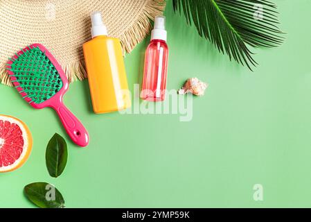 Stylish female accessories, hair brush, straw hat and sunblock, sunscreen cosmetic products for hair care on green background with tropical leaves, co Stock Photo