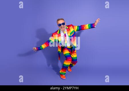 Vibrant senior man in rainbow suit enjoys disco vibes on a stunning violet backdrop Stock Photo