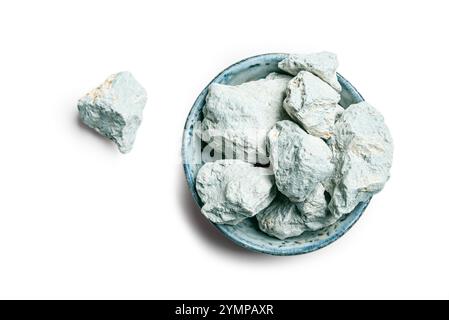 Piece of edible kaolin clay in bowl isolated on white background, top view. Blue clay stones. Stock Photo