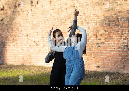 Two female dancers are practicing a modern dance choreography in an urban setting with a brick wall in the background Stock Photo