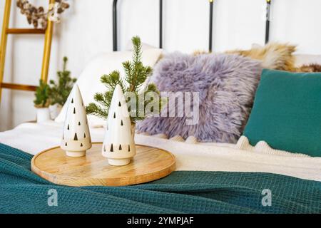 Ceramic decorative trees and soft textiles in tranquil bedroom setting background. Two ceramic Christmas trees on wooden tray, surrounded by plush pil Stock Photo