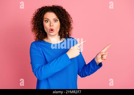Young woman with vibrant hair in blue sweater pointing with surprise against pink background Stock Photo