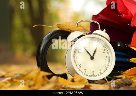 Autumn time. Alarm clock and umbrella in park, closeup Stock Photo
