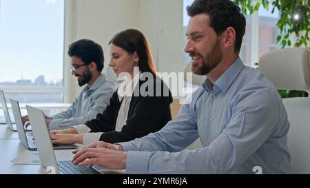Row of diverse smiling business people businessmen and businesswoman typing on laptops professional colleagues team of technical support staff members Stock Photo