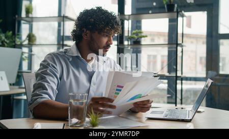 Stressed sad Arabian Indian man anxious male worker executive manager working at office check paperwork commerce on laptop upset businessman hold Stock Photo