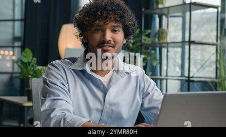 Business portrait Indian arabian man smiling male businessman cheerful guy gen z working on laptop computer studying online at office ethnic hispanic Stock Photo