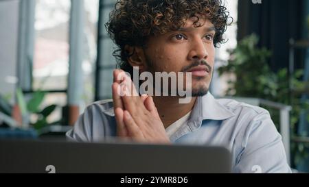 Thoughtful male guy Indian Arabian businessman office manager ceo entrepreneur employee work laptop doubtful latino man think decision solve problem Stock Photo